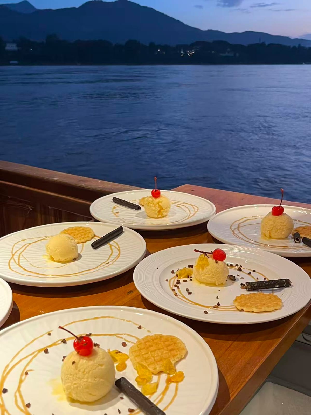 Desserts on plates with a scenic view of water and mountains in the background