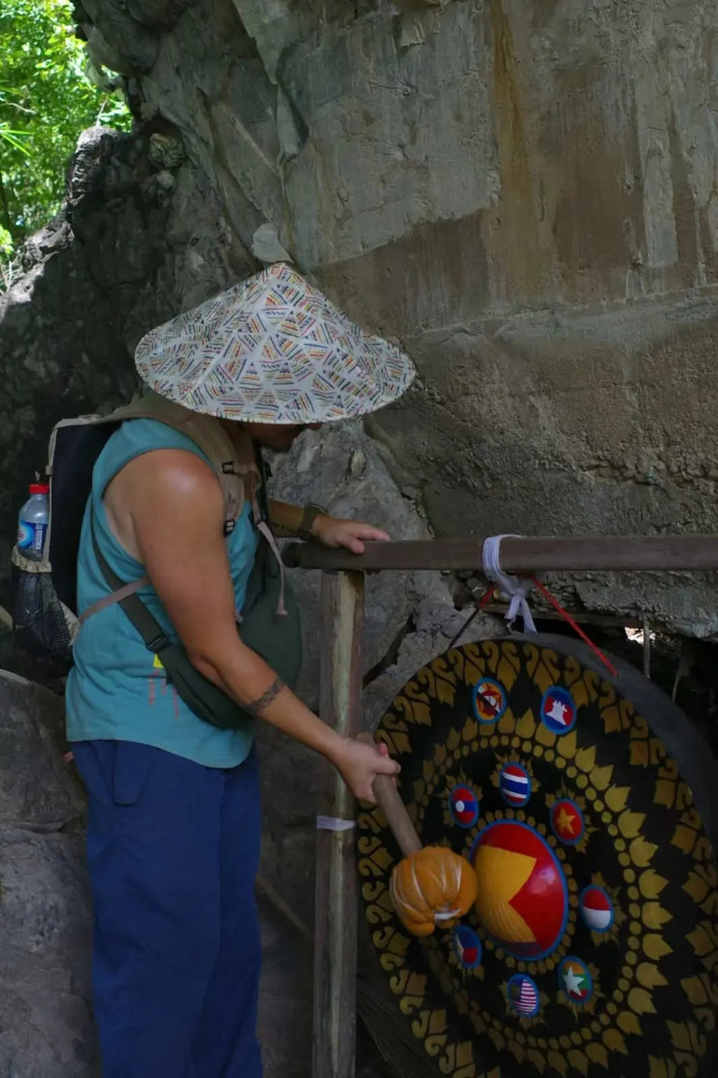 Person wearing a conical hat interacting with a colorful wheel of fortune against a stone wall.